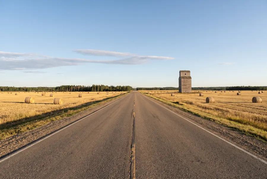 Two-lane highway through harvested fields and a grain elevator